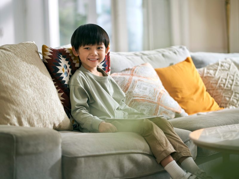 Little,Asian,Boy,Sitting,On,Family,Couch,In,Living,Room